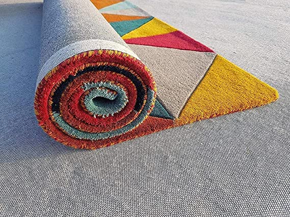Natural wool rug with a soft textured pile and colourful geometric pattern in red, yellow, blue and grey, shown rolled on a floor.